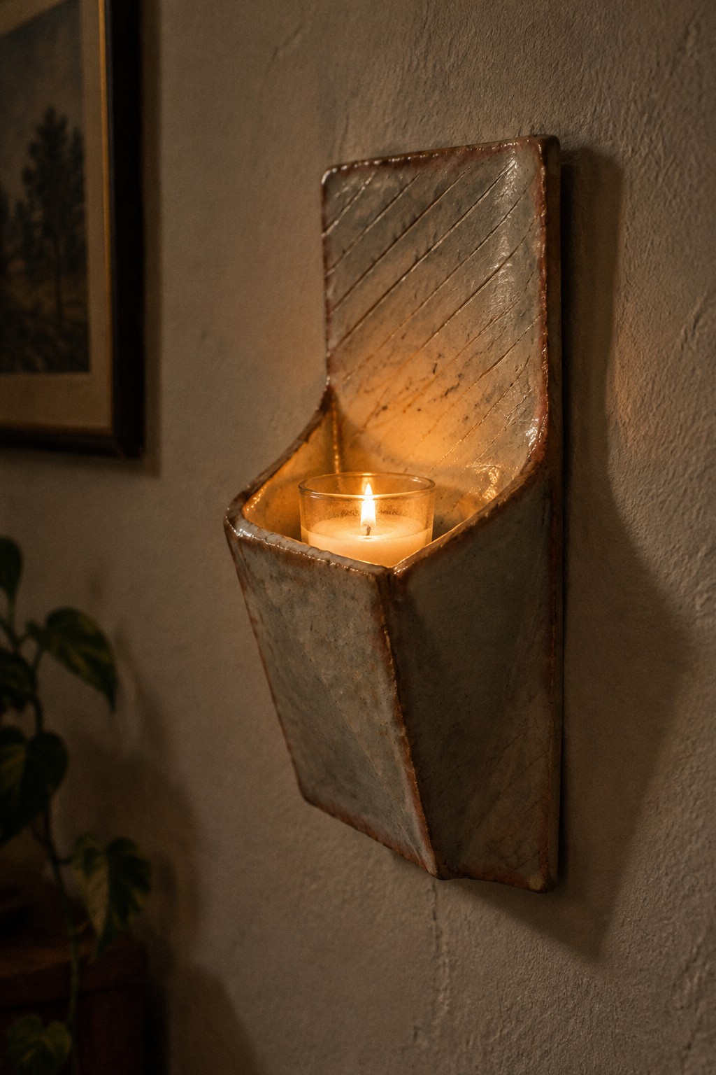 Rustic ceramic wall sconce with diagonal patterns holding a lit candle in glass.
