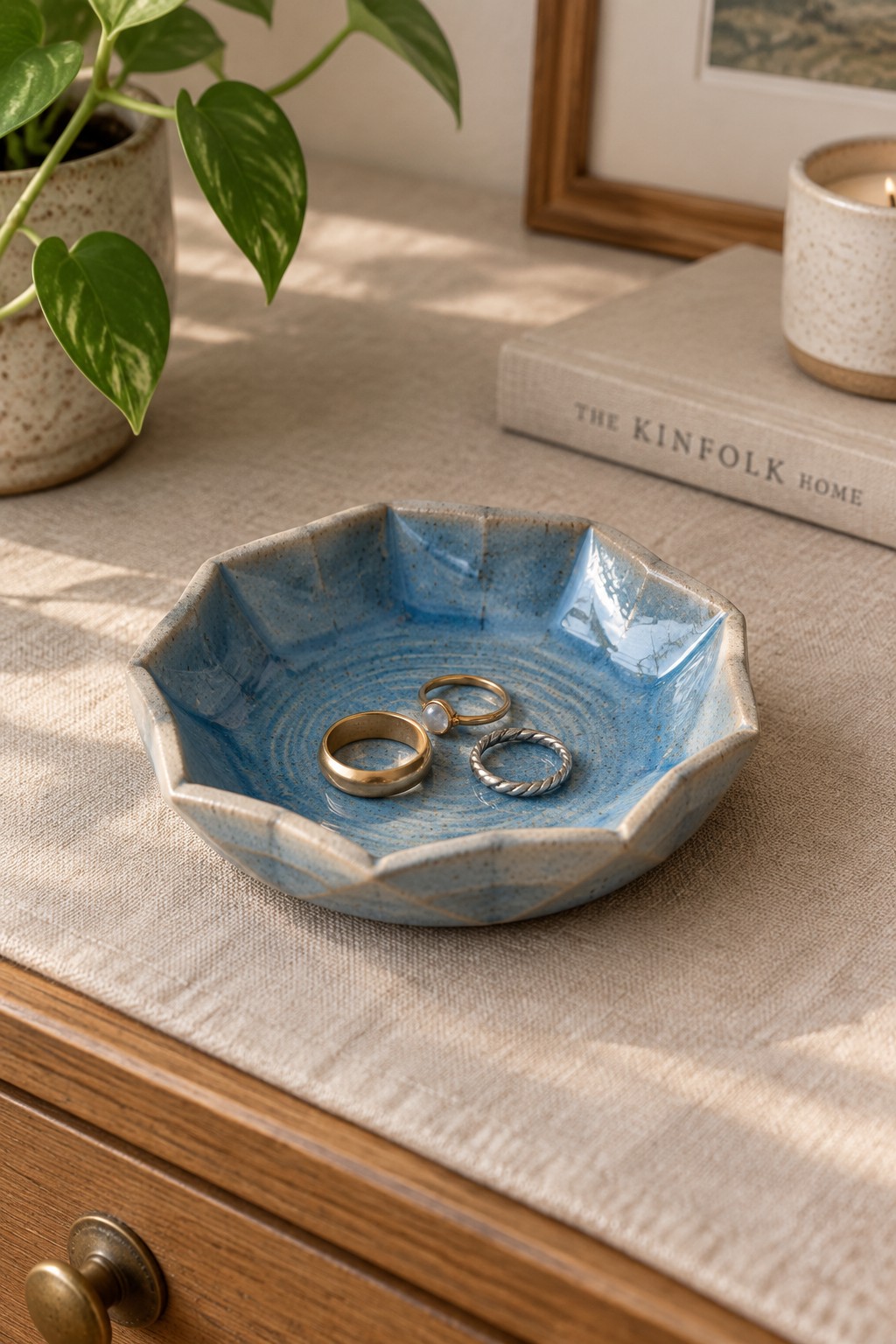 Blue scalloped ceramic bowl holding three rings on linen-covered wood
