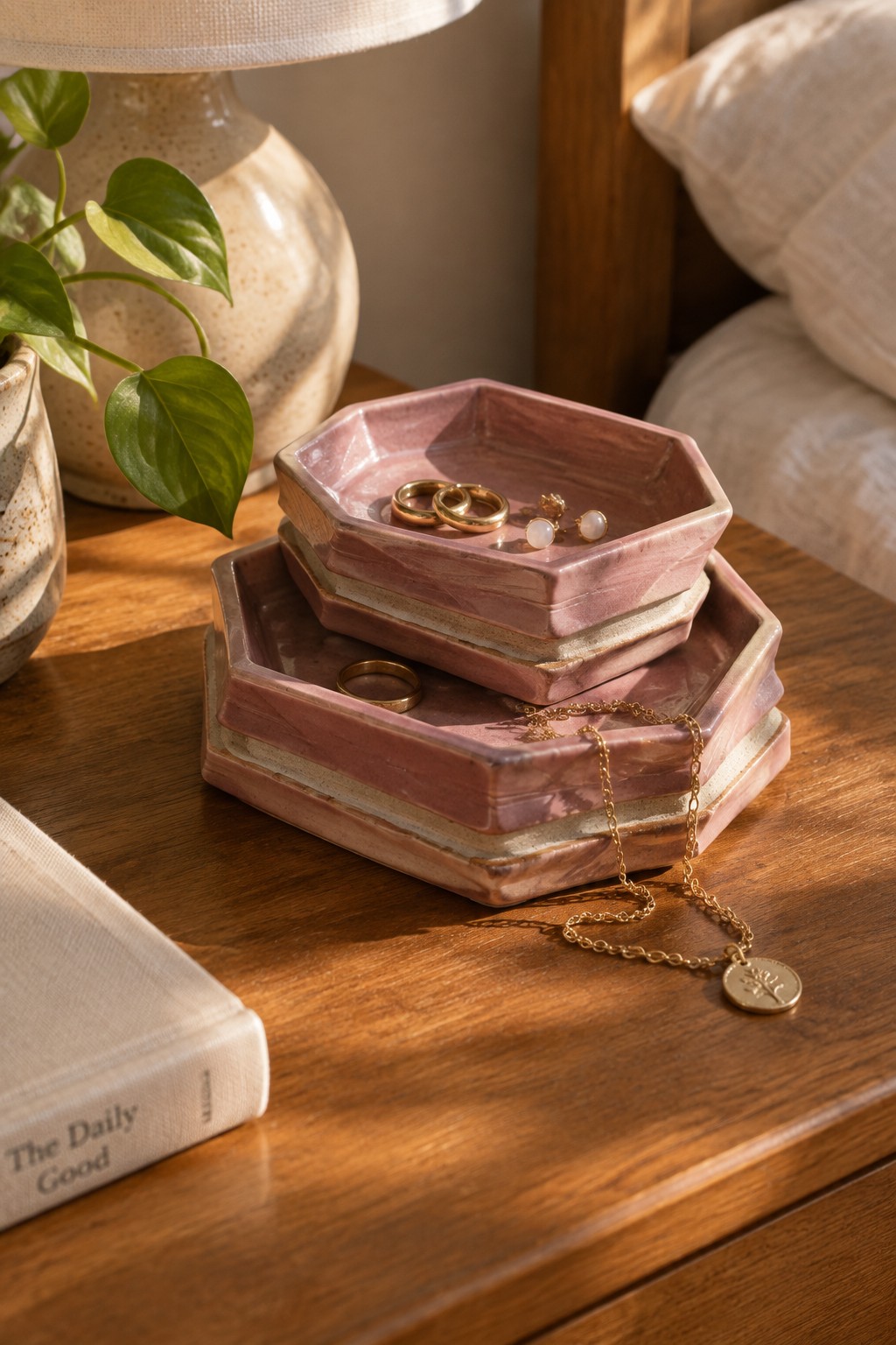 Stacked pink hexagonal trays with gold jewelry on wooden bedside table