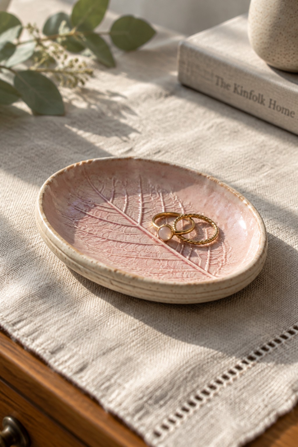 Pink leaf-shaped ceramic dish holding two gold rings on linen fabric