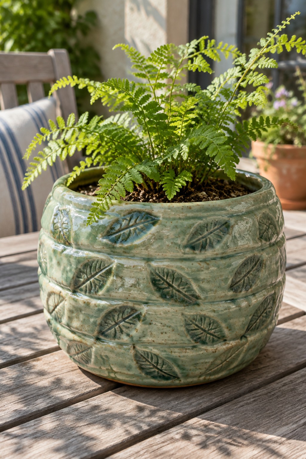 Lush fern in green ceramic pot with leaf patterns on wooden table