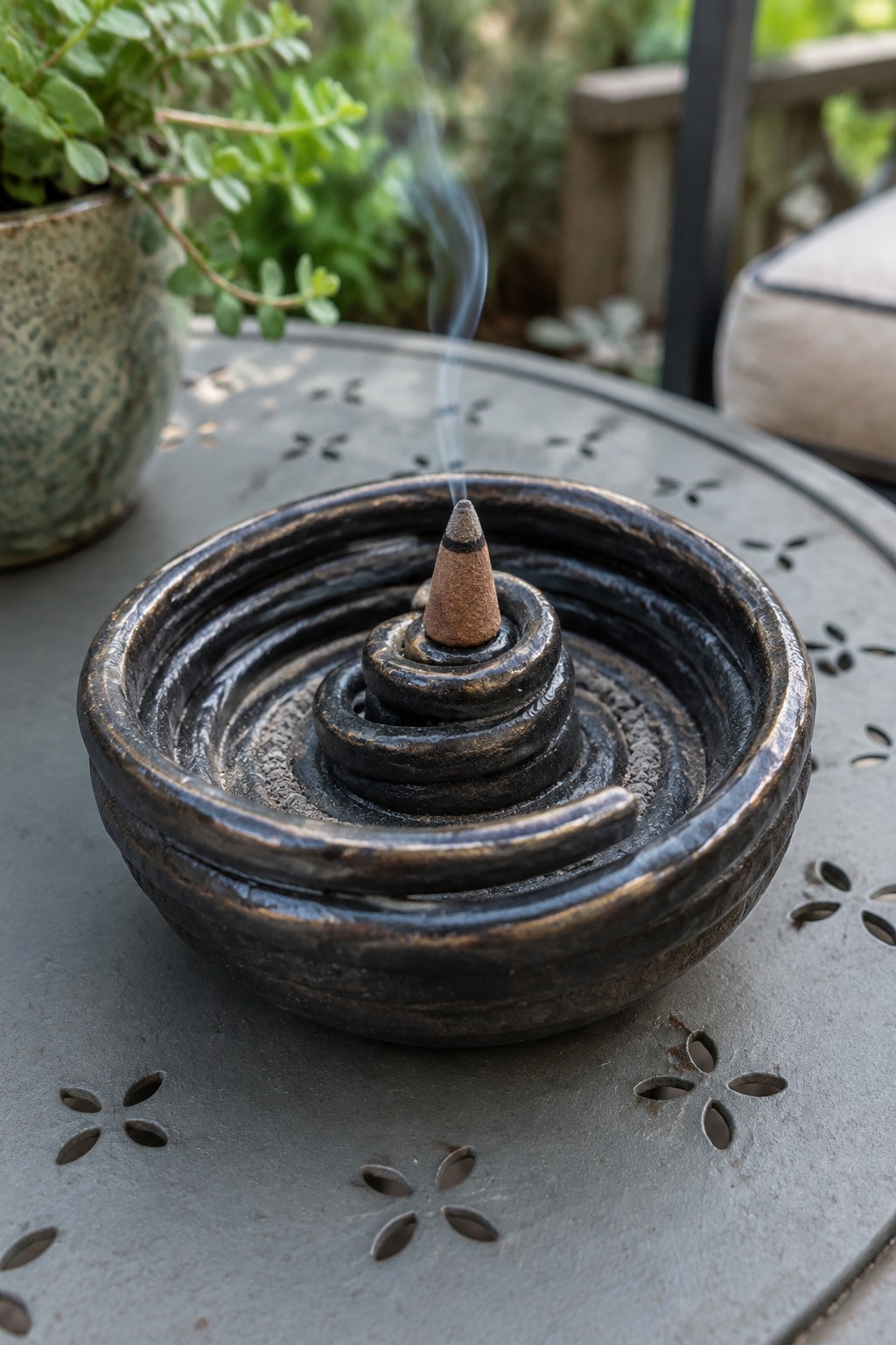 Burning incense cone in dark spiral ceramic holder on metal table with rising smoke