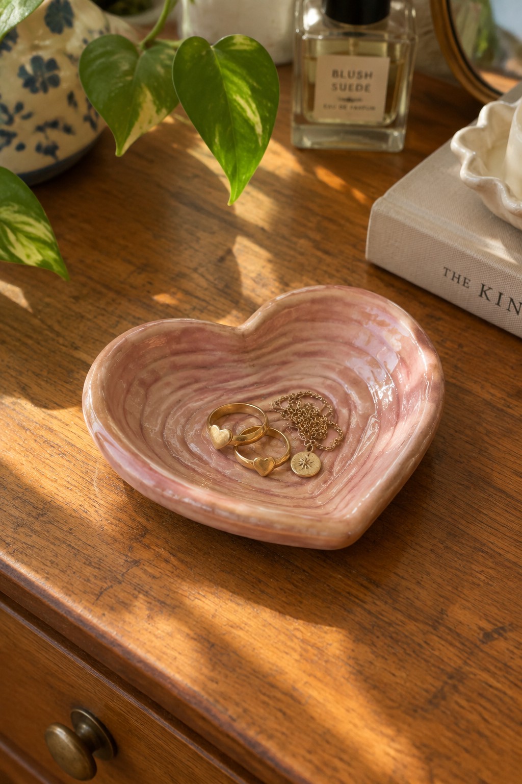 Pink marbled heart bowl with gold rings and sun necklace on wooden table