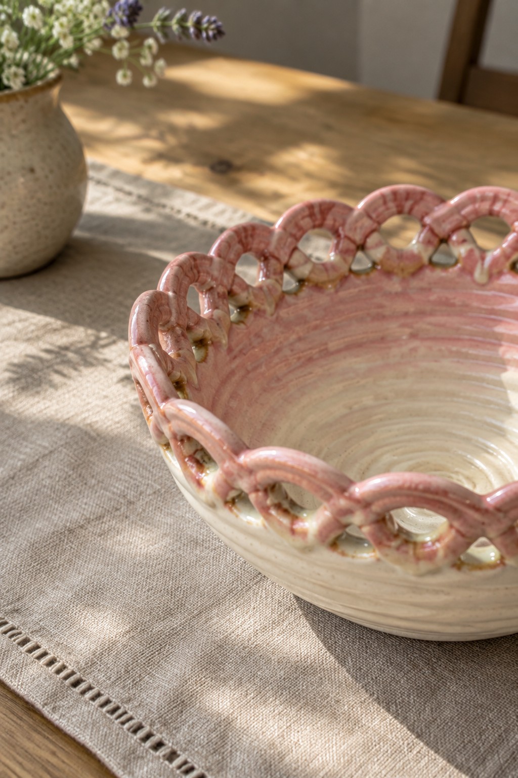 Pink ceramic bowl with looped rim on linen over wooden table