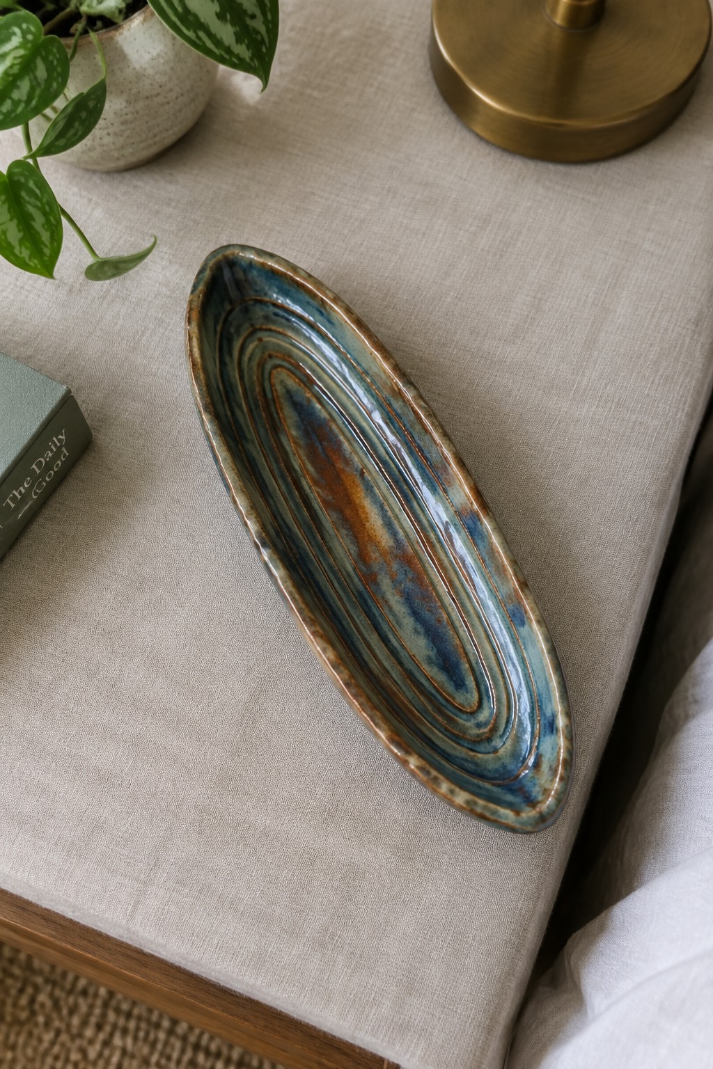 Blue and brown glazed ceramic oval dish on beige linen with potted plant
