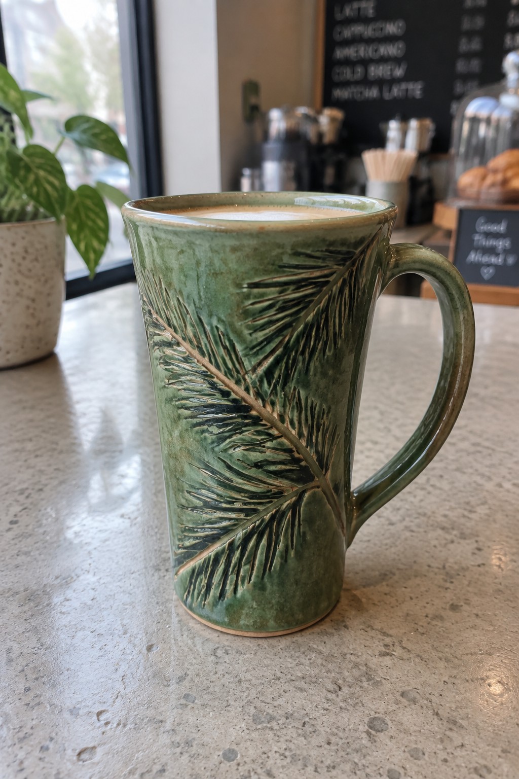 Green ceramic mug with embossed fern design holding coffee on cafe counter