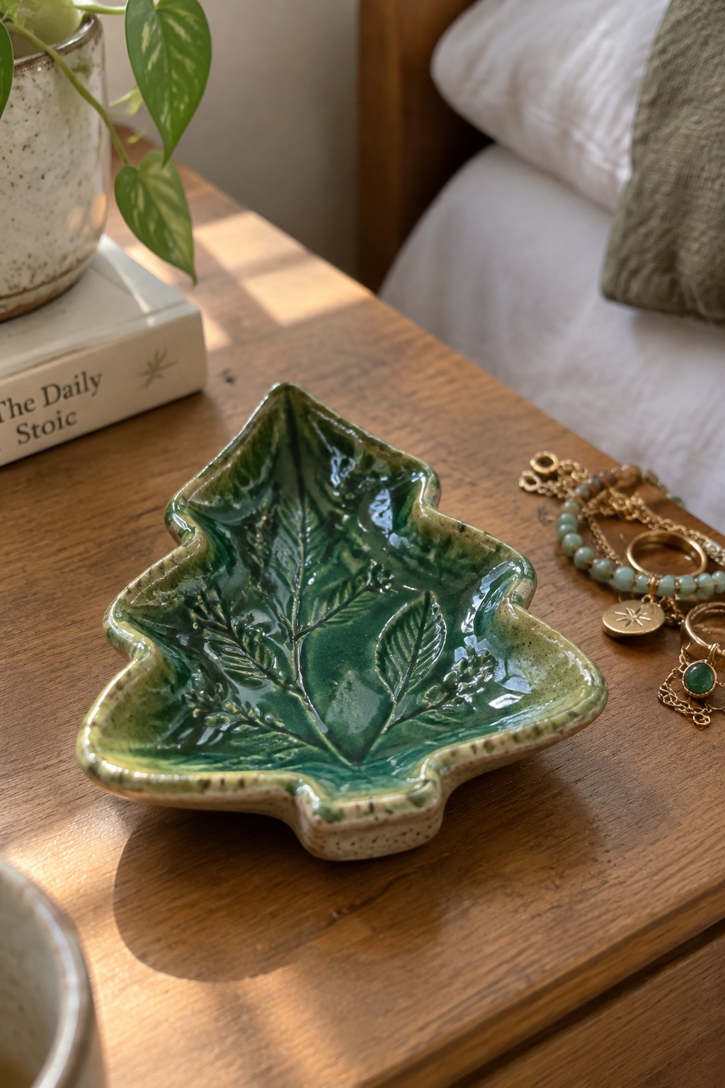Green ceramic leaf dish on wooden table beside jewelry and plant