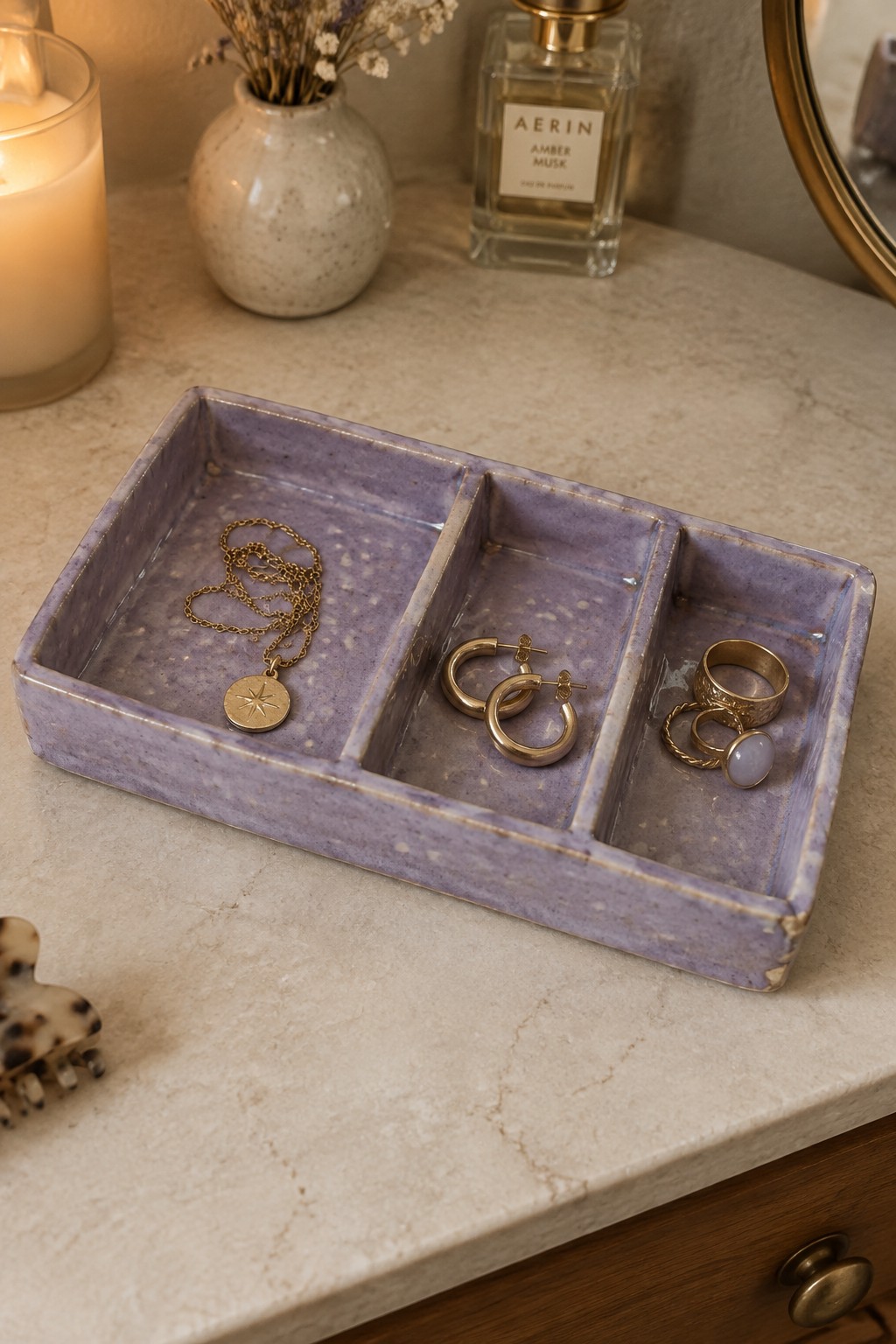 Purple ceramic tray with gold necklace, hoop earrings and rings on marble vanity.