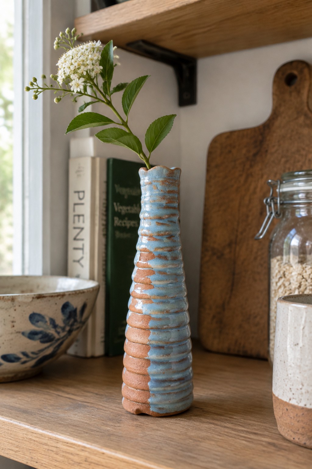 Blue and terracotta ribbed vase with white flowers on wooden shelf with books
