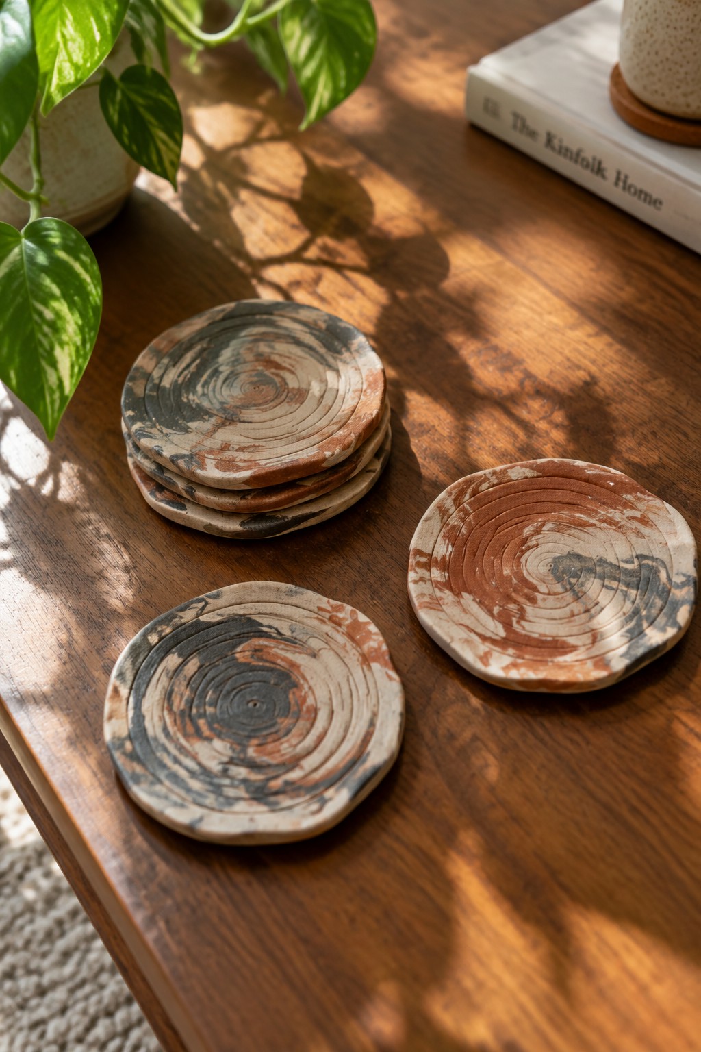 Marbled ceramic coasters on wooden table beside potted plant and book in sunlight