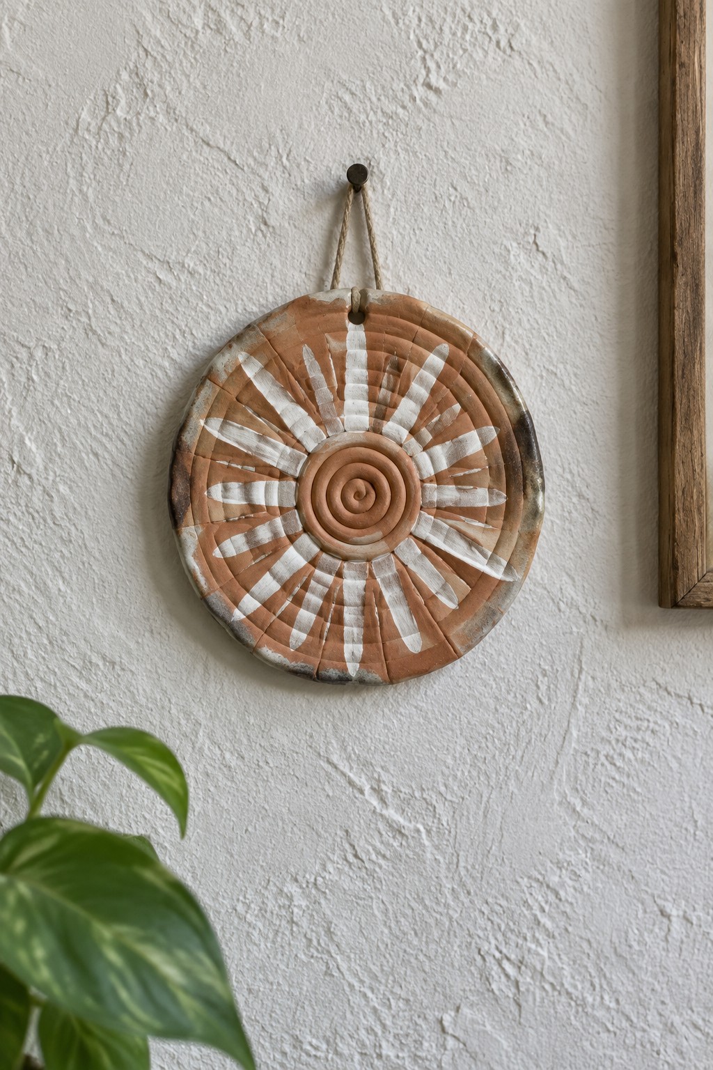 Terracotta sunburst wall hanging with white spiral design on textured wall