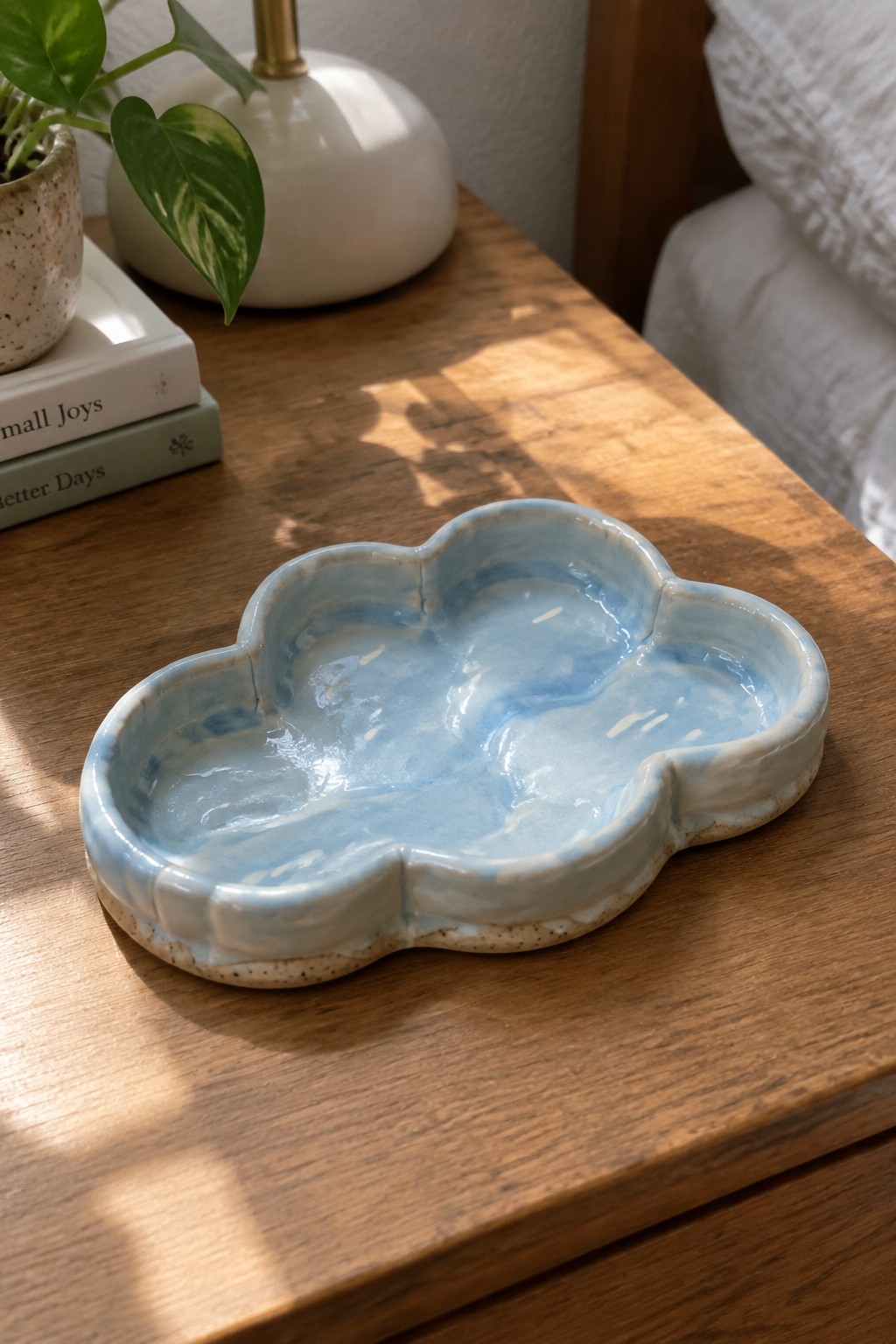 Blue cloud-shaped ceramic tray on sunlit wooden bedside table with books and plant