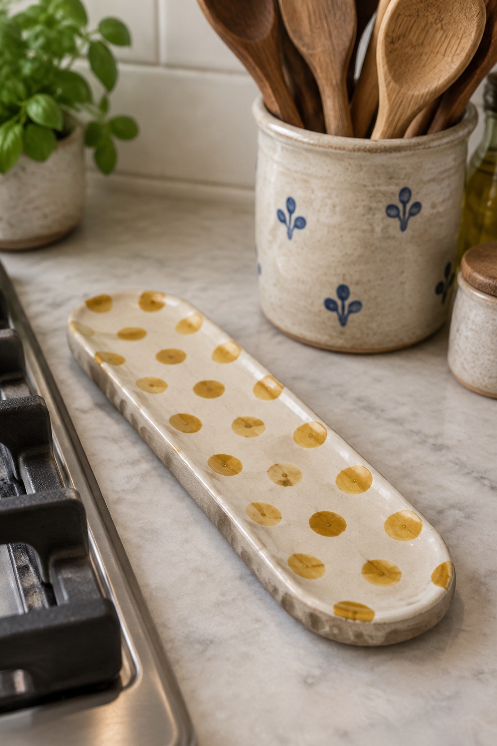Gold-dotted ceramic tray beside blue-patterned crock of wooden spoons on marble counter