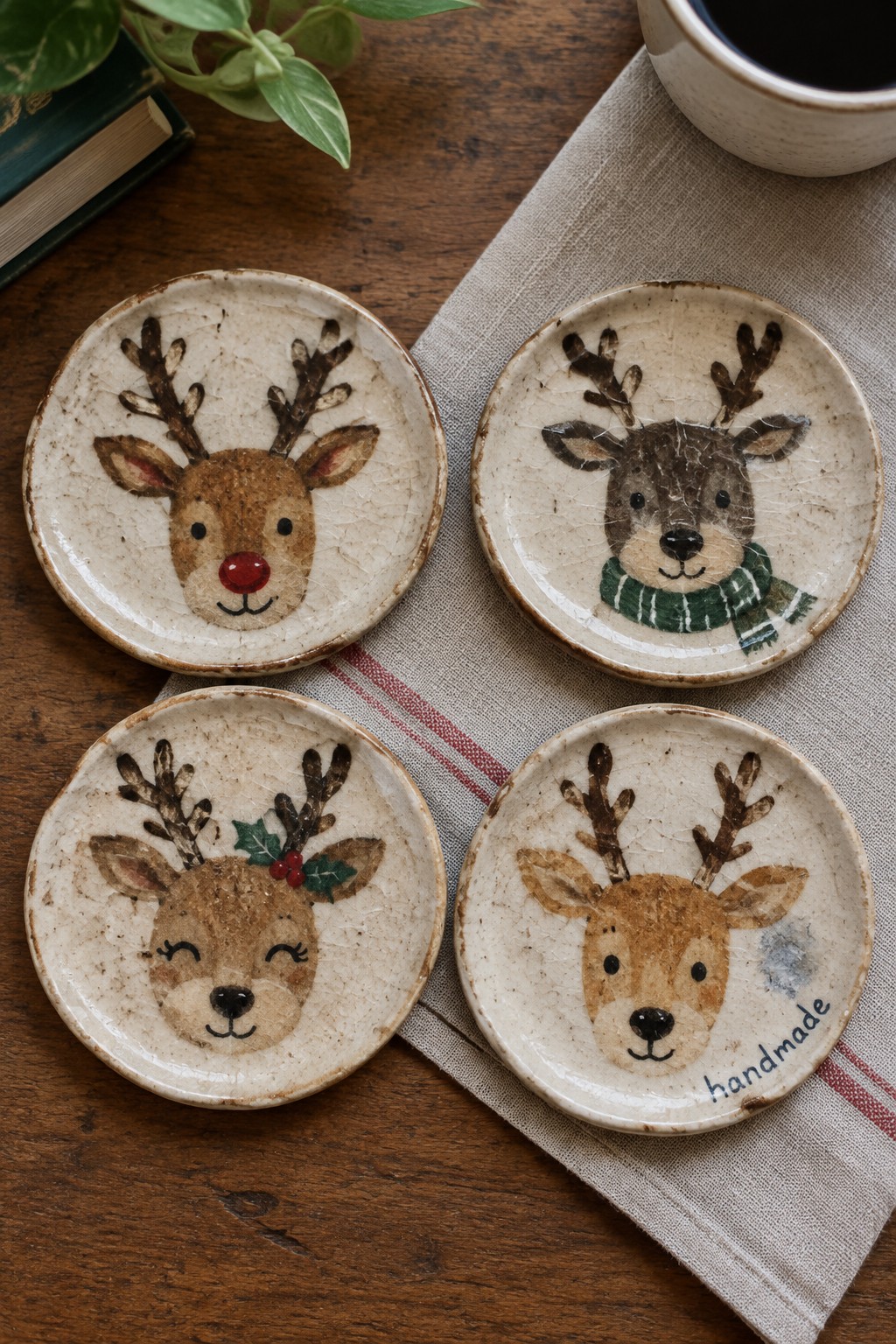 Four crackled ceramic plates with painted reindeer faces on wooden table with linen.