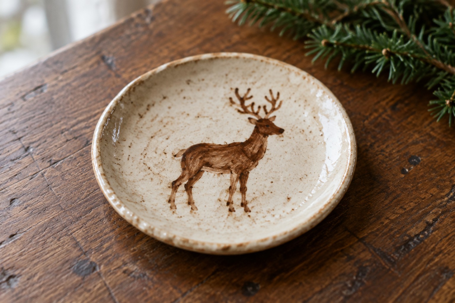 Rustic ceramic plate with brown deer illustration on wooden table beside pine branch.