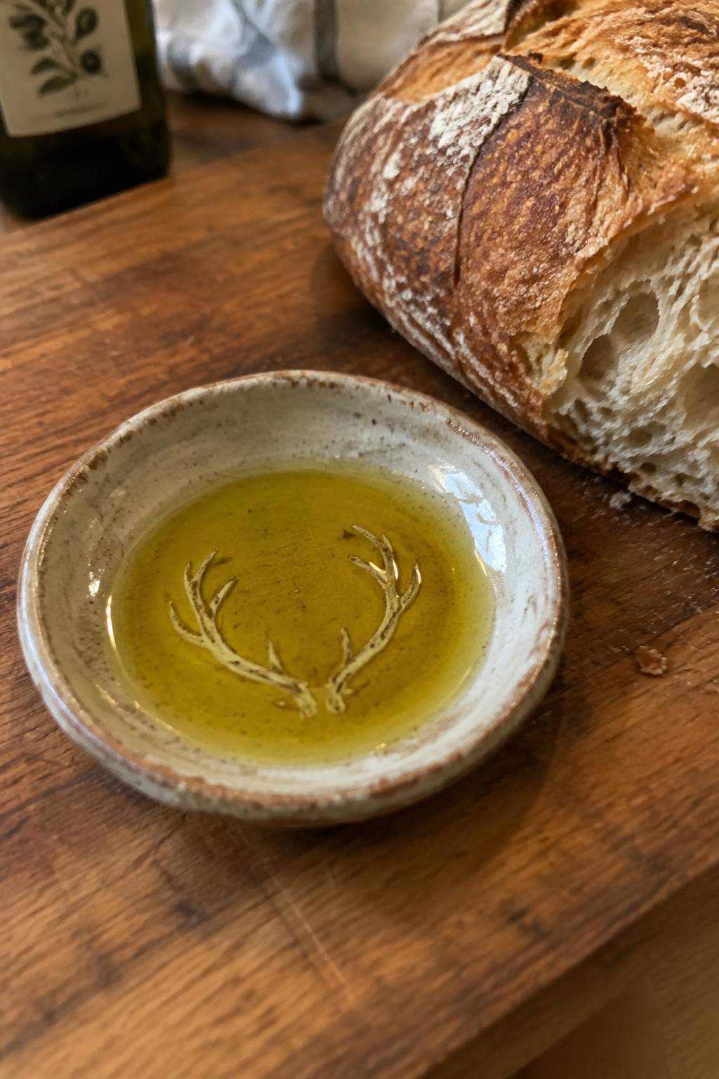 Small ceramic bowl of olive oil beside crusty sourdough bread on wooden table