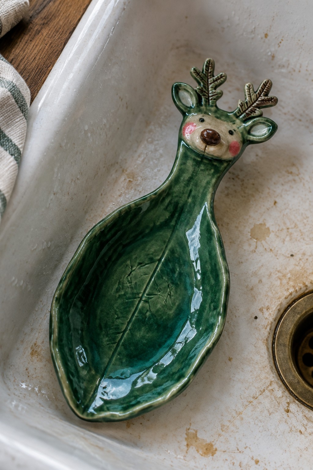 Green ceramic reindeer spoon rest in stained white kitchen sink