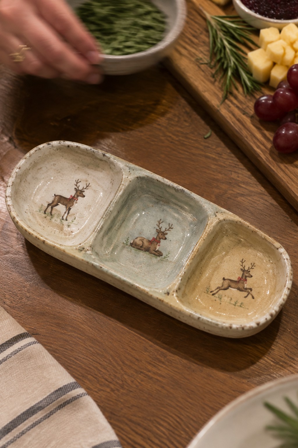 Ceramic three-section dish with deer illustrations on wooden table beside cheese and grapes