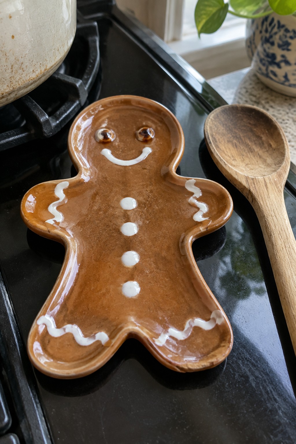 Brown glazed gingerbread man ceramic dish with white icing details beside wooden spoon on stove