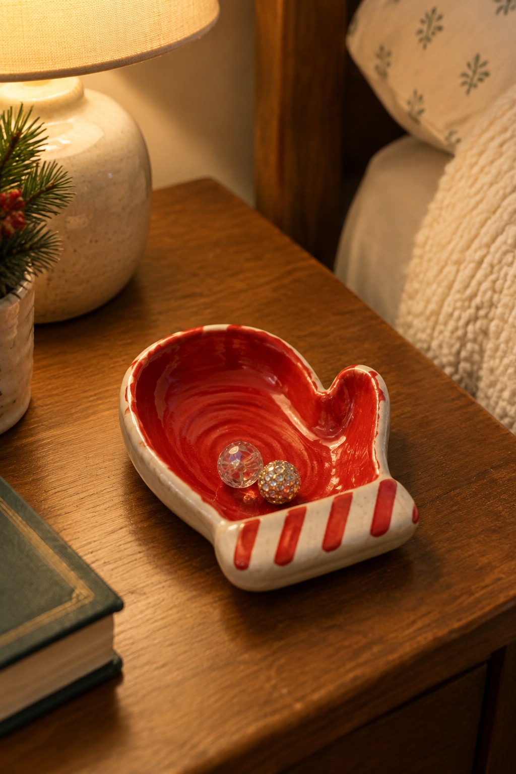 Red ceramic mitten dish holding two sparkly ornaments on wooden nightstand