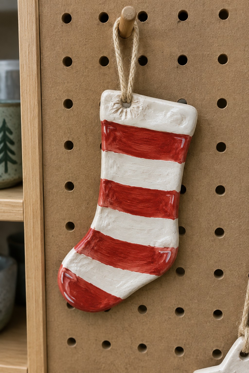 Red and white striped ceramic Christmas stocking hanging on pegboard hook