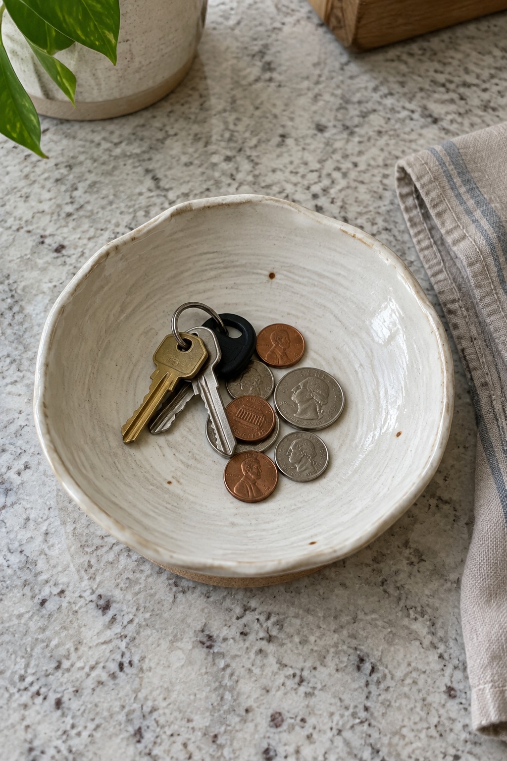 White ceramic bowl with keys and coins on speckled marble countertop