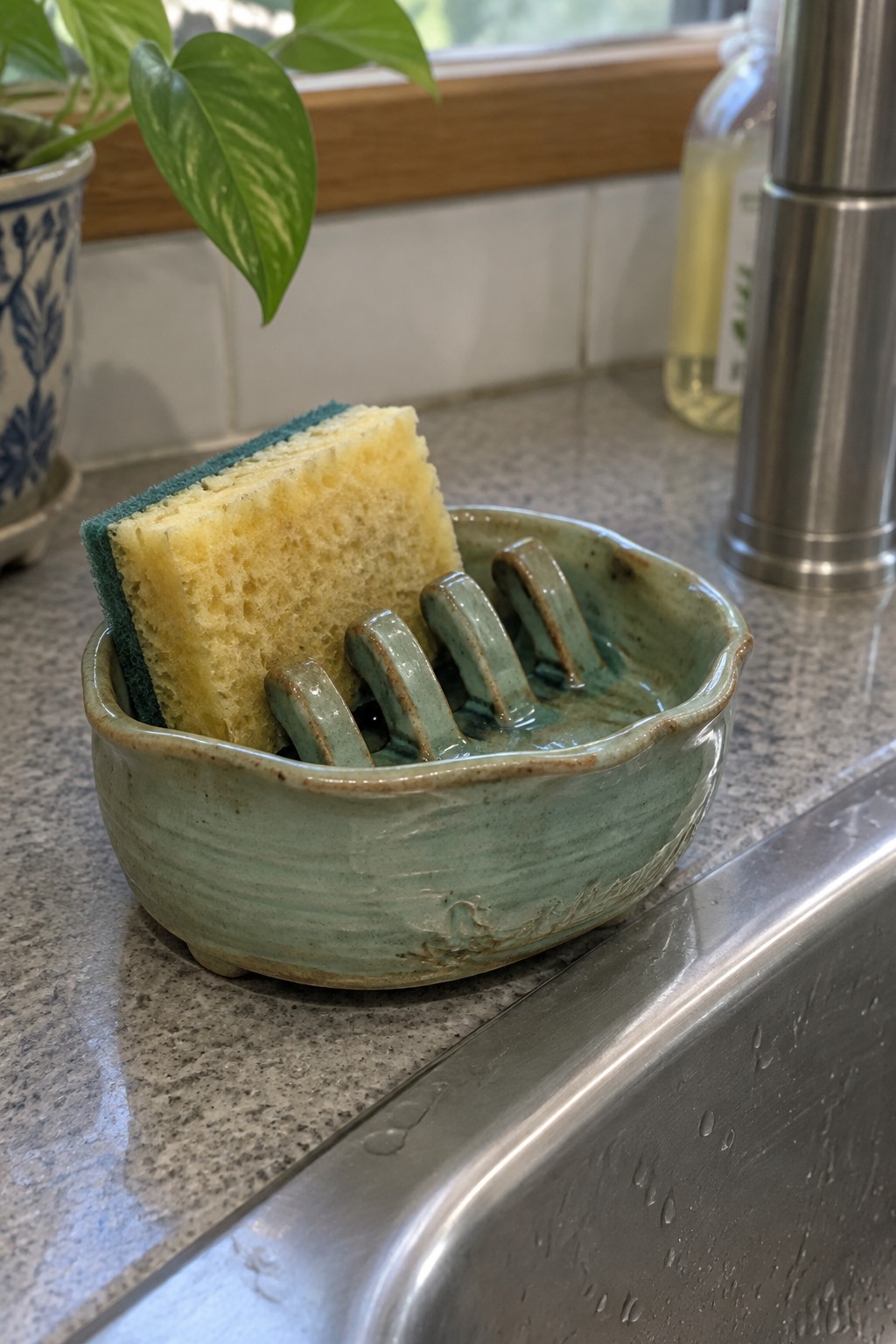 Yellow sponge in ridged green ceramic dish on kitchen countertop by sink
