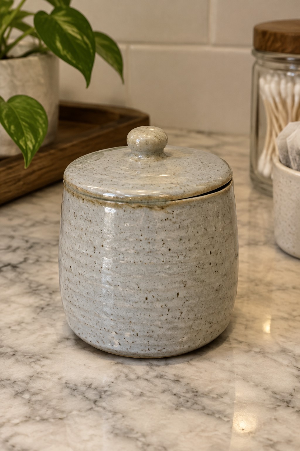 Speckled ceramic jar with lid on white marble countertop near potted plant