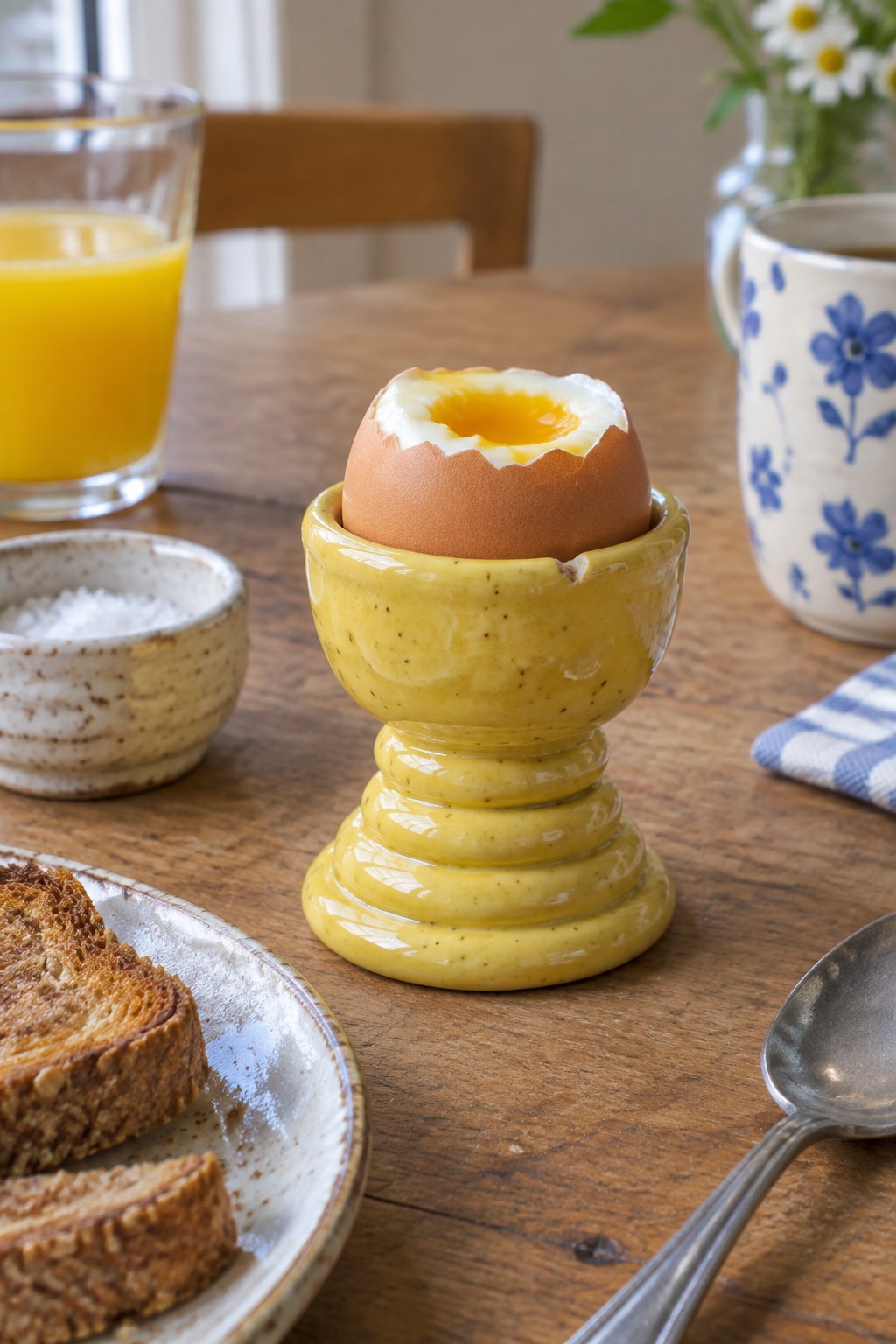 Soft-boiled egg with runny yolk in yellow cup beside toast and orange juice