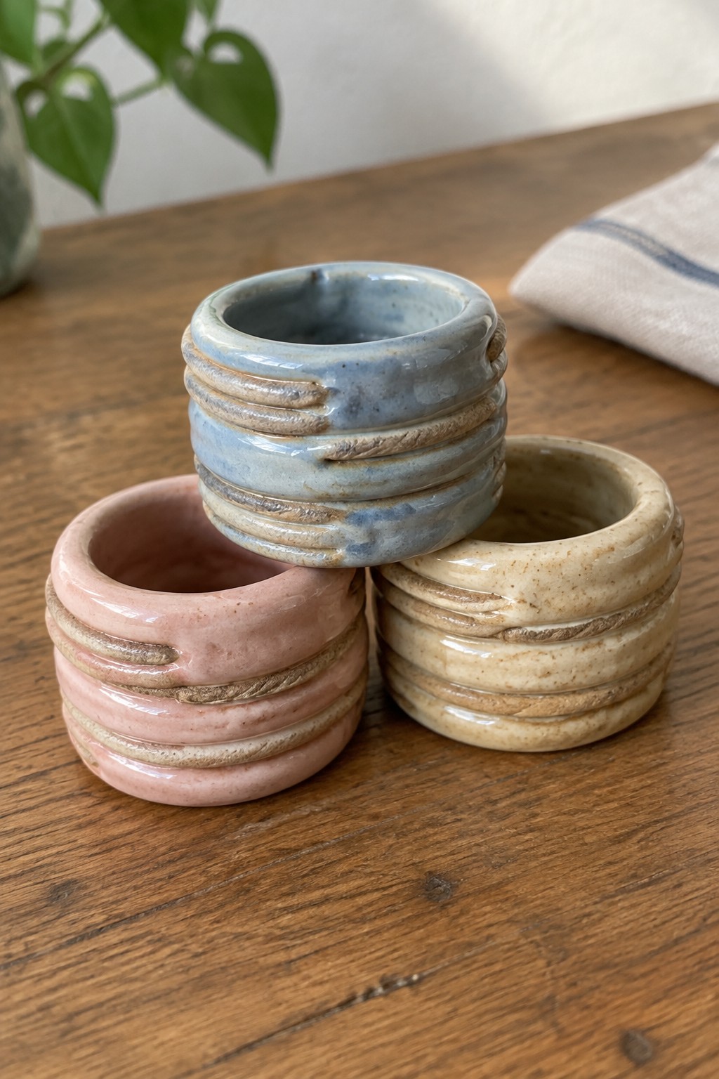 Three stacked ceramic rings in pink, blue, and beige on wooden table.