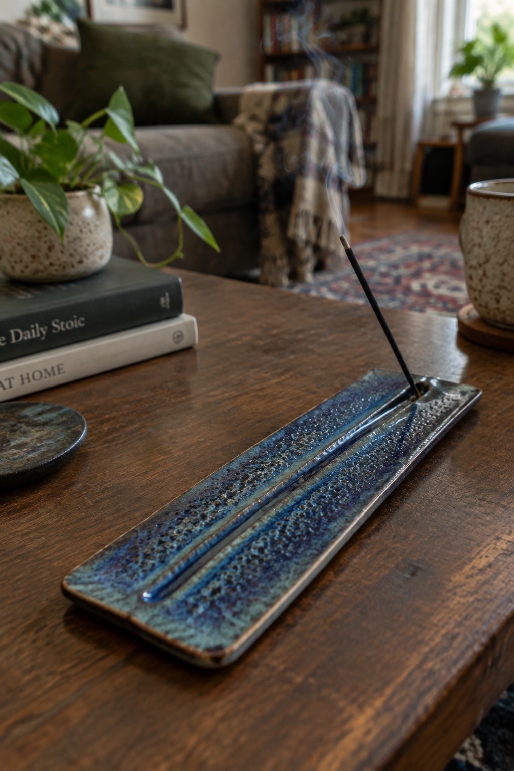 Incense burning in long blue ceramic holder on wooden table with books and plant