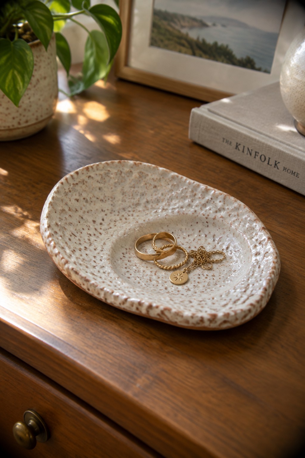 Speckled ceramic bowl with gold rings and star pendant necklace on wood