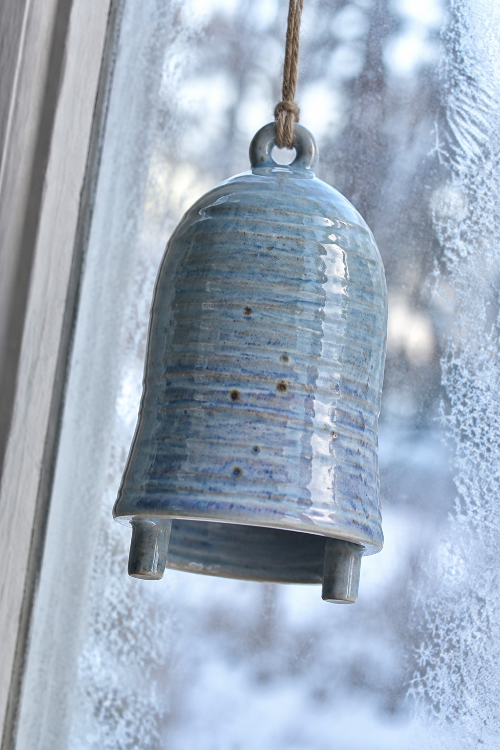 Blue ceramic bell hanging from rope against frosted snowy window