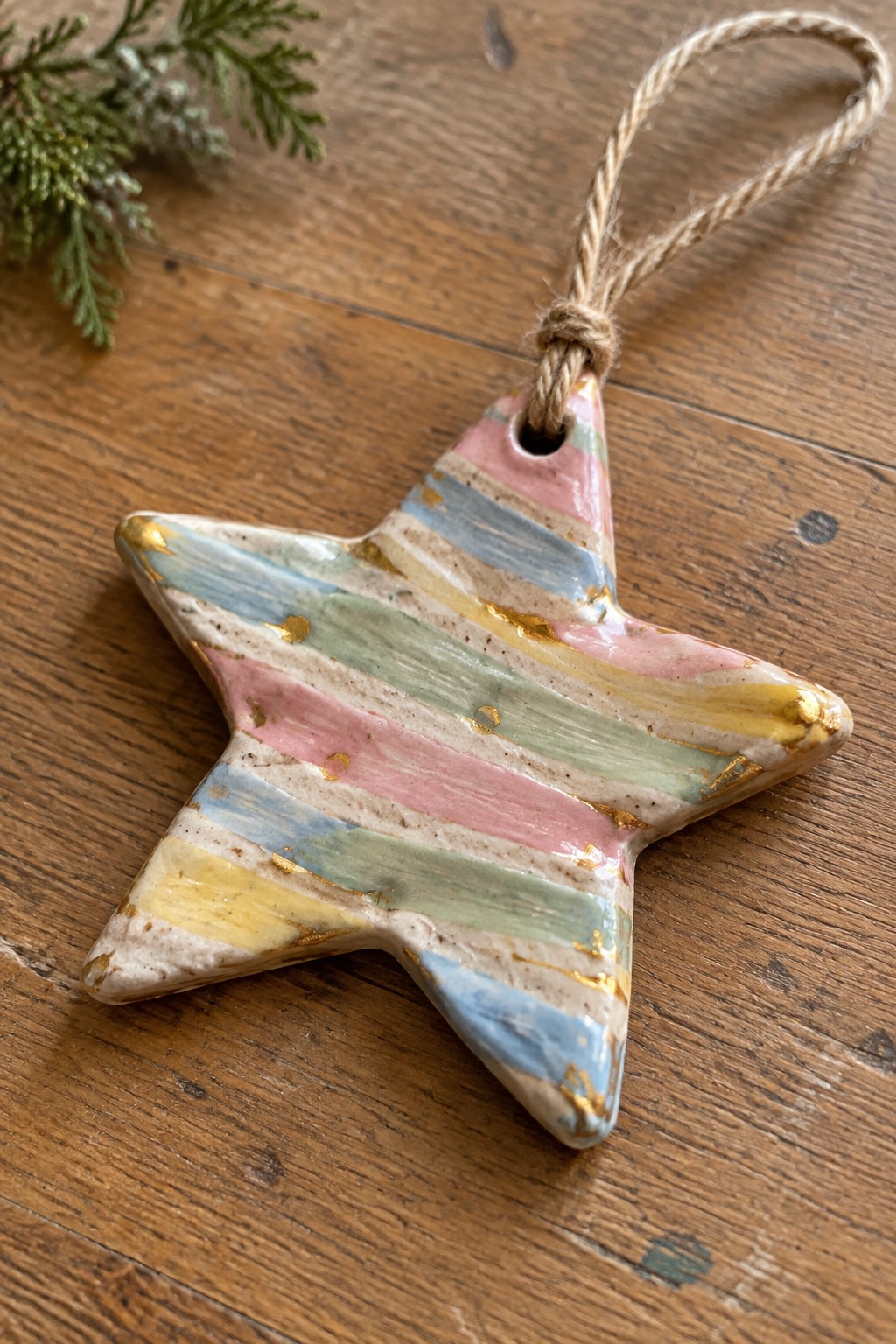 Pastel-striped ceramic star ornament with gold accents hanging by twine on wood.