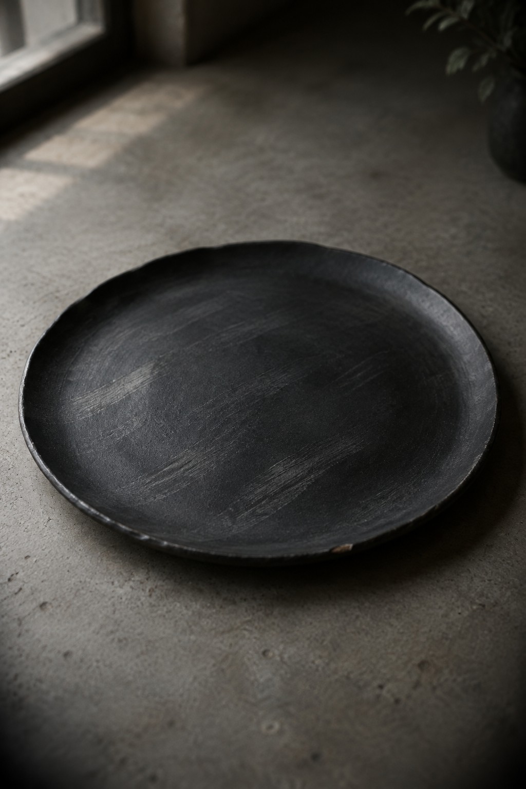 Dark matte black ceramic plate on gray concrete floor with soft light.