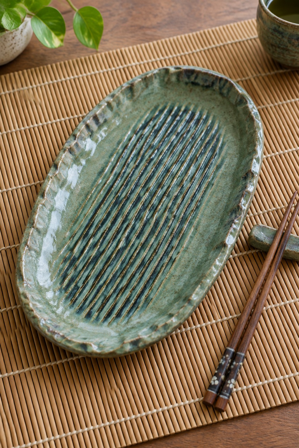 Green ridged ceramic plate on bamboo mat with chopsticks and cup