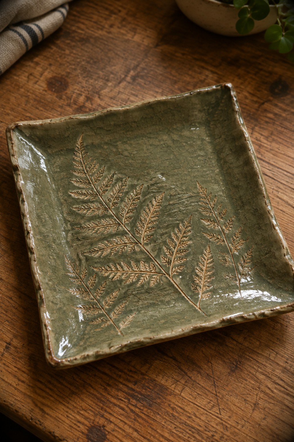 Green square ceramic dish with embossed ferns on rustic wooden table