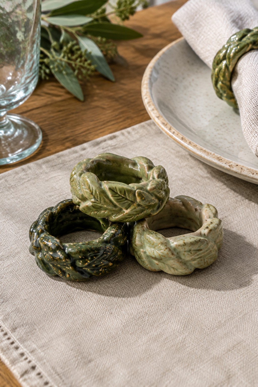 Three green ceramic napkin rings with leaf designs on beige linen cloth