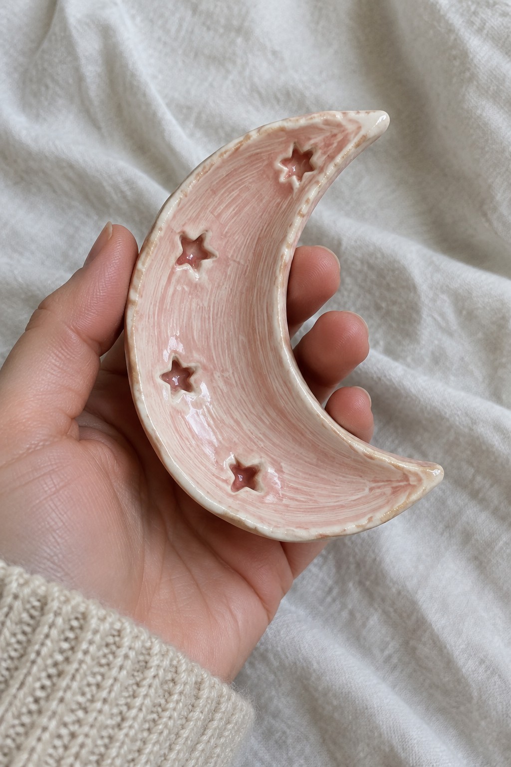 Hand in beige knit sweater holding pink ceramic crescent moon with star cutouts