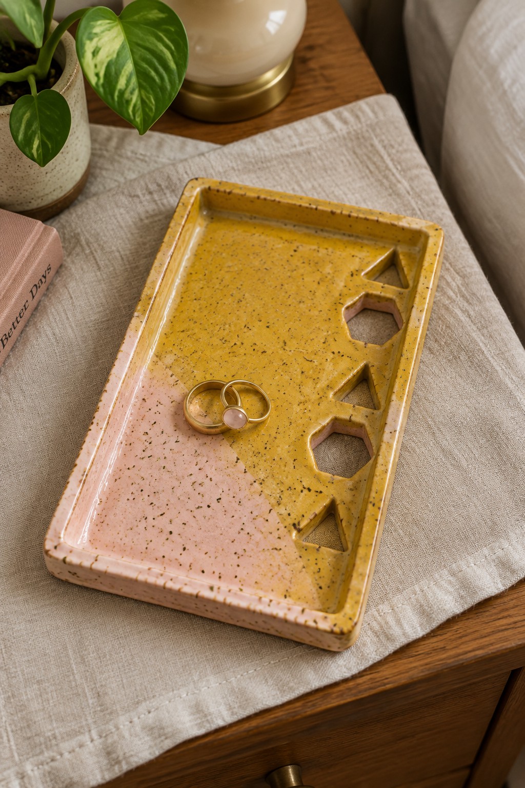 Two gold rings on pink-and-yellow speckled ceramic tray with geometric cutouts