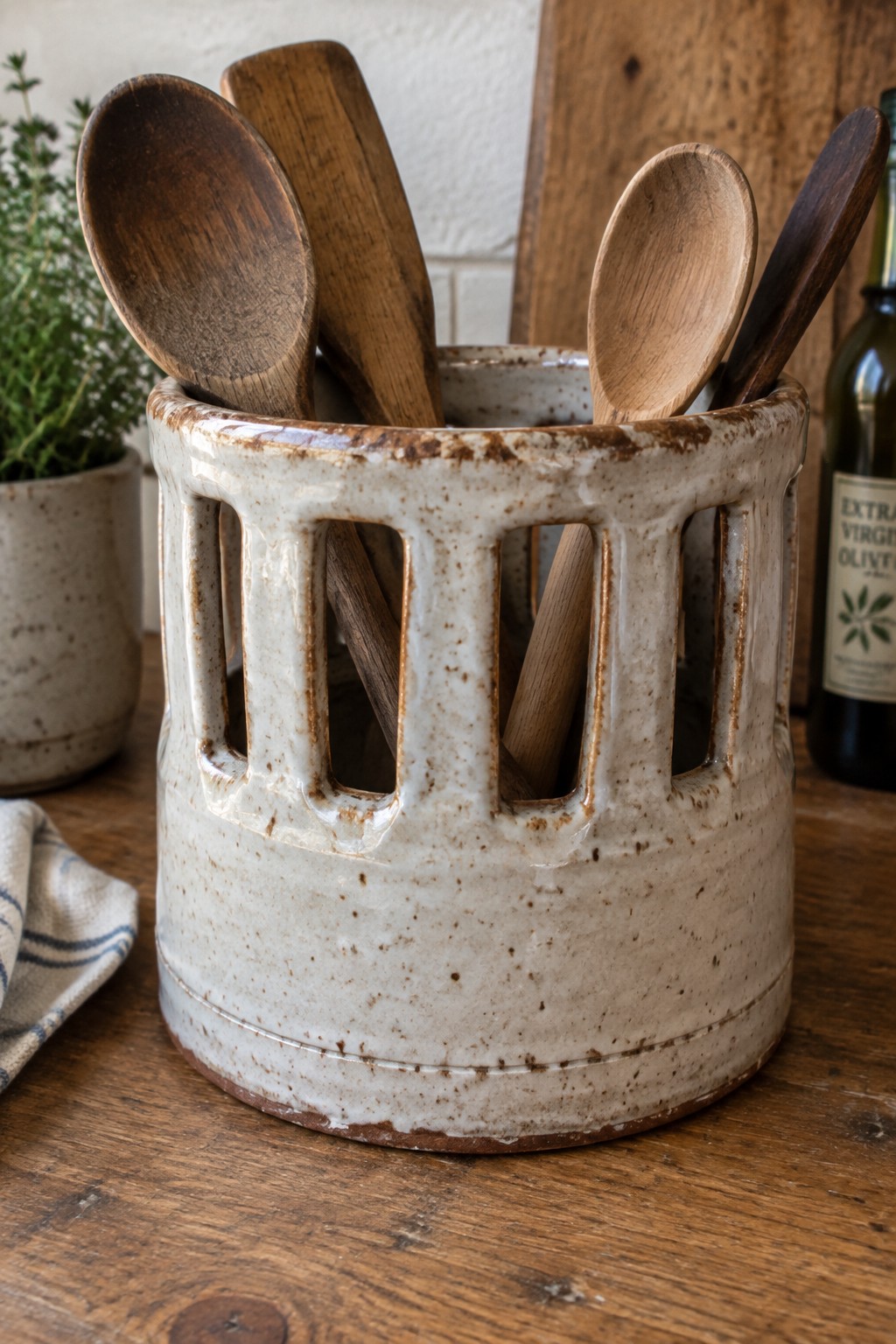 Speckled ceramic crock with cutouts holding wooden spoons on rustic kitchen counter