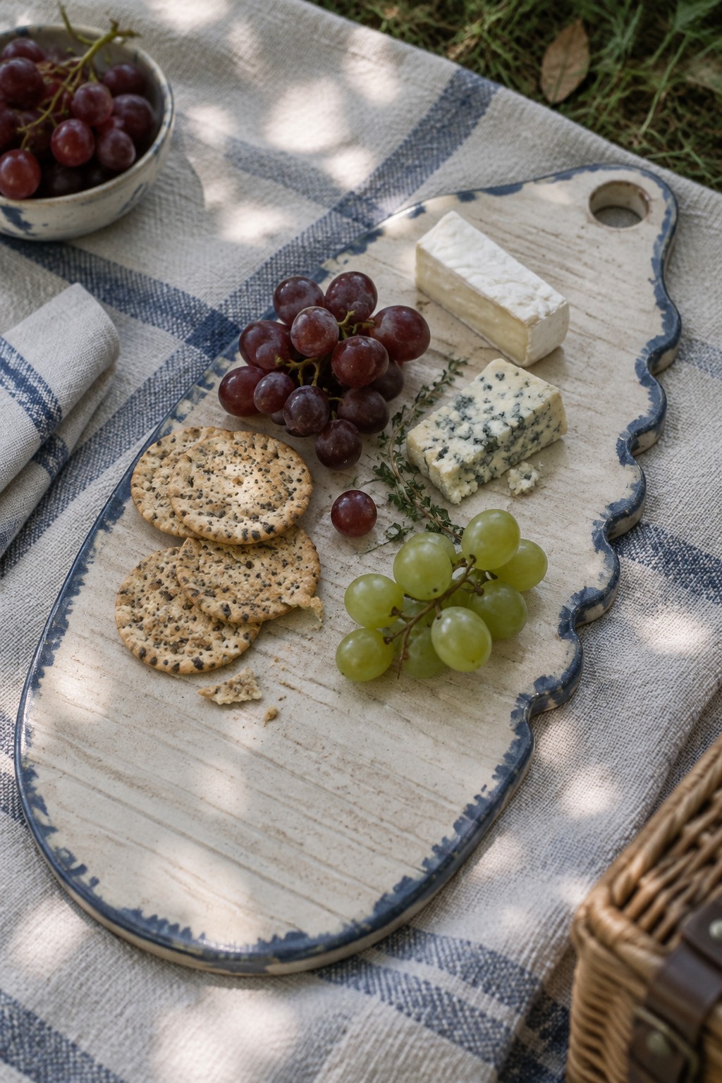 Cheese board with crackers, red and green grapes, brie and blue cheese on checkered blanket