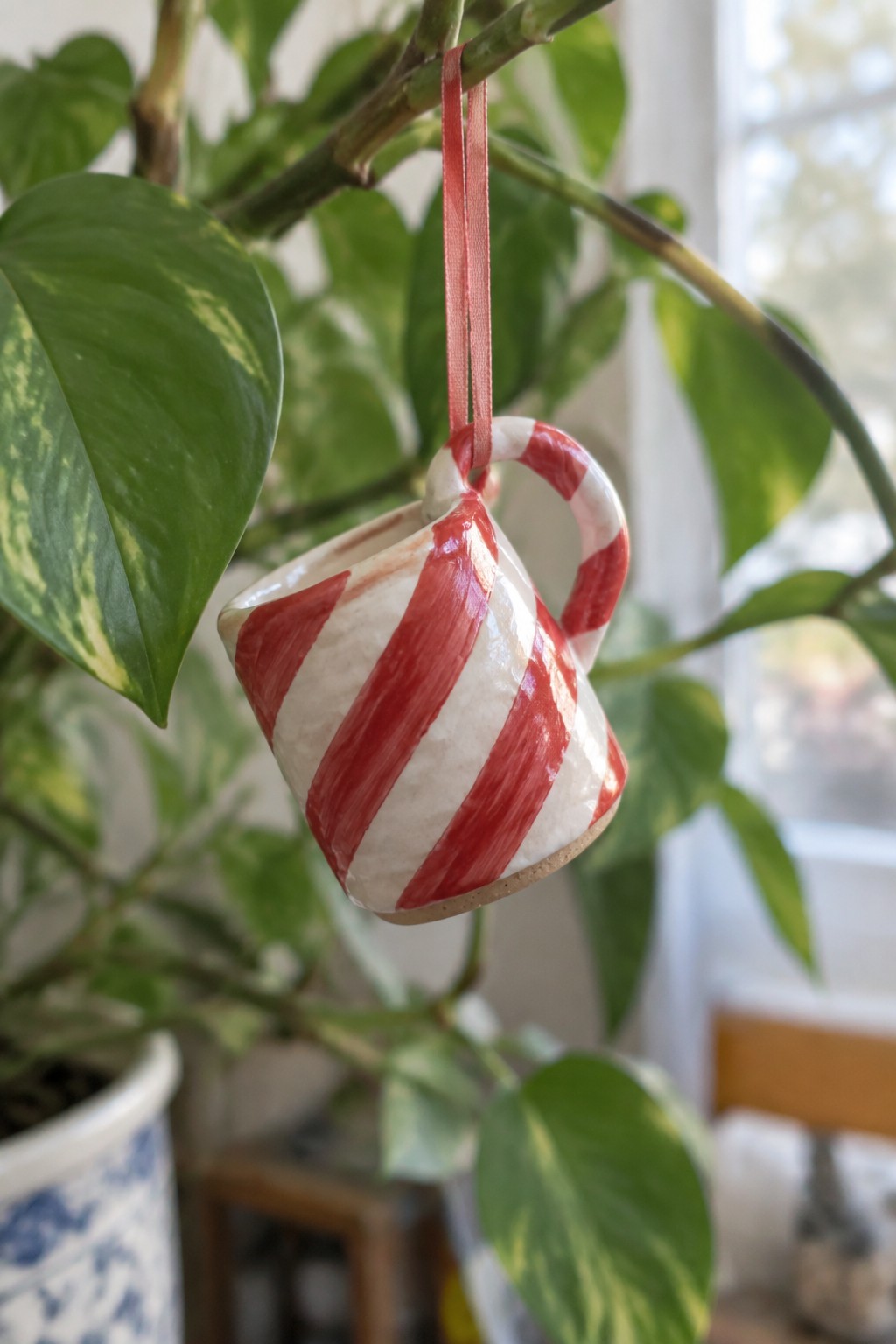 Miniature white ceramic mug with red stripes hanging by red ribbon from plant branch