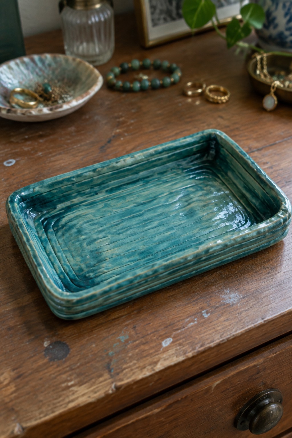 Teal ceramic tray with ridged glaze on rustic wooden dresser amid jewelry