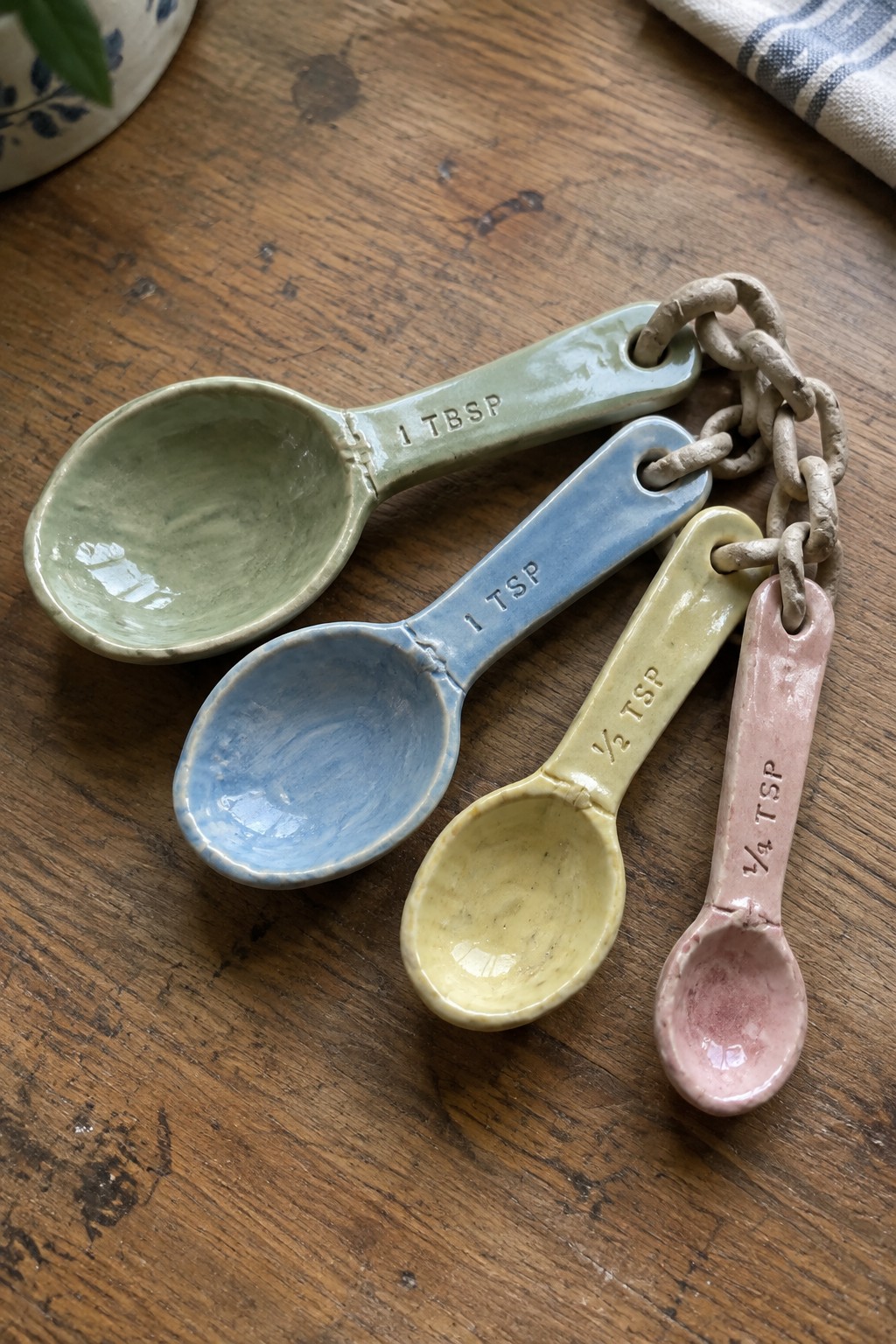 Pastel ceramic measuring spoons chained together on wooden table