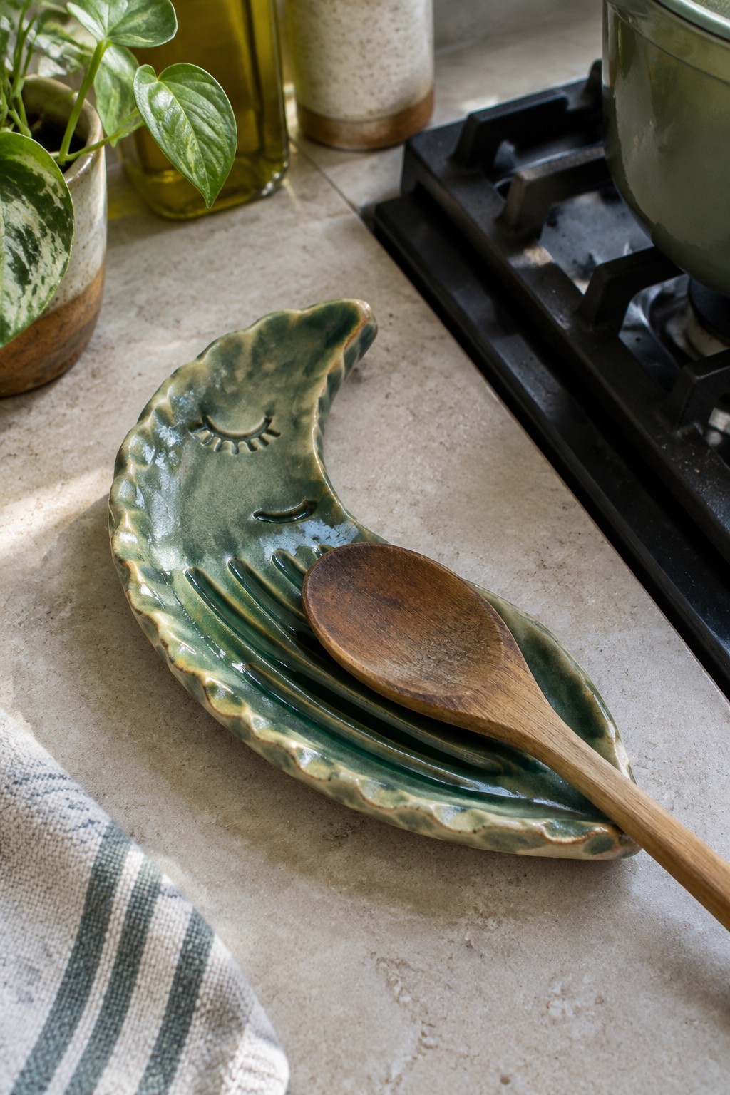 Green ceramic moon-shaped dish with face holding wooden spoon and fork on counter