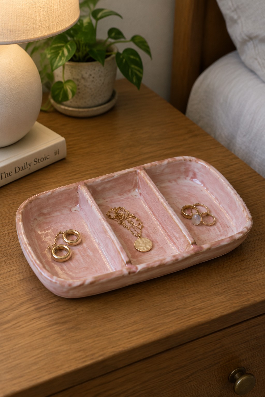 Pink marbled three-section tray holding gold jewelry on wooden nightstand