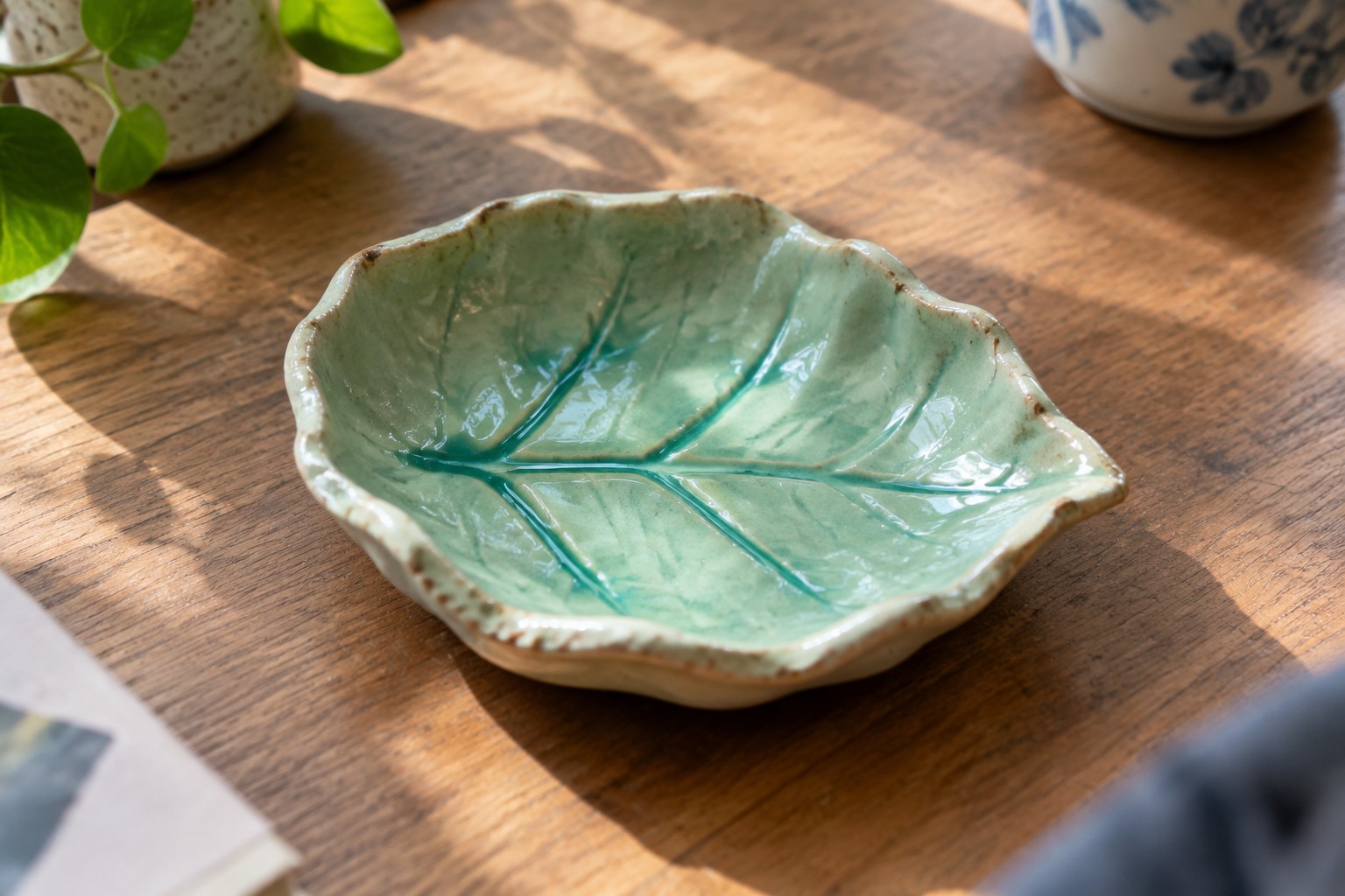Green ceramic leaf dish holding gold ring and flower earrings on wooden table