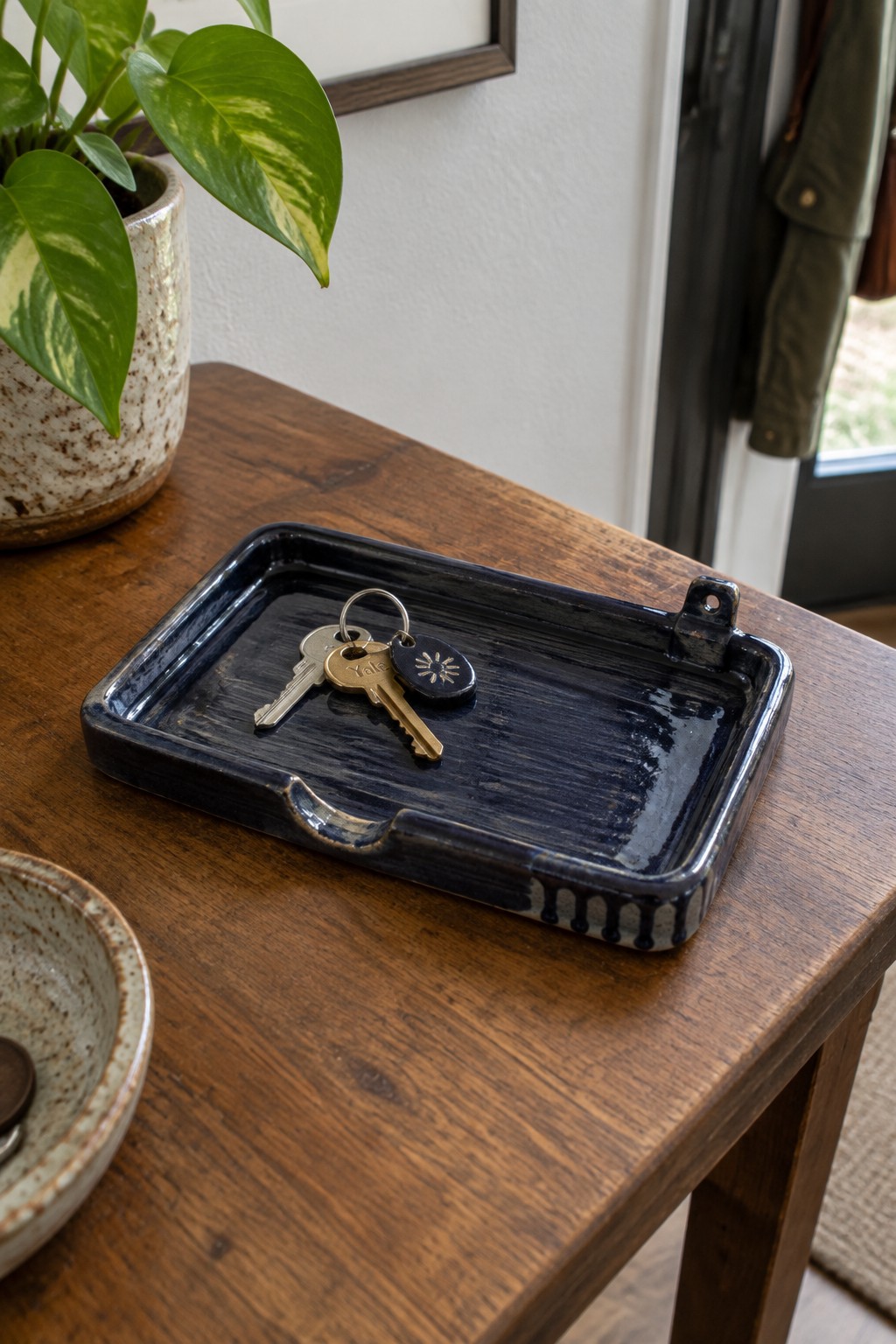 Dark blue ceramic tray with keys on wooden table beside potted plant