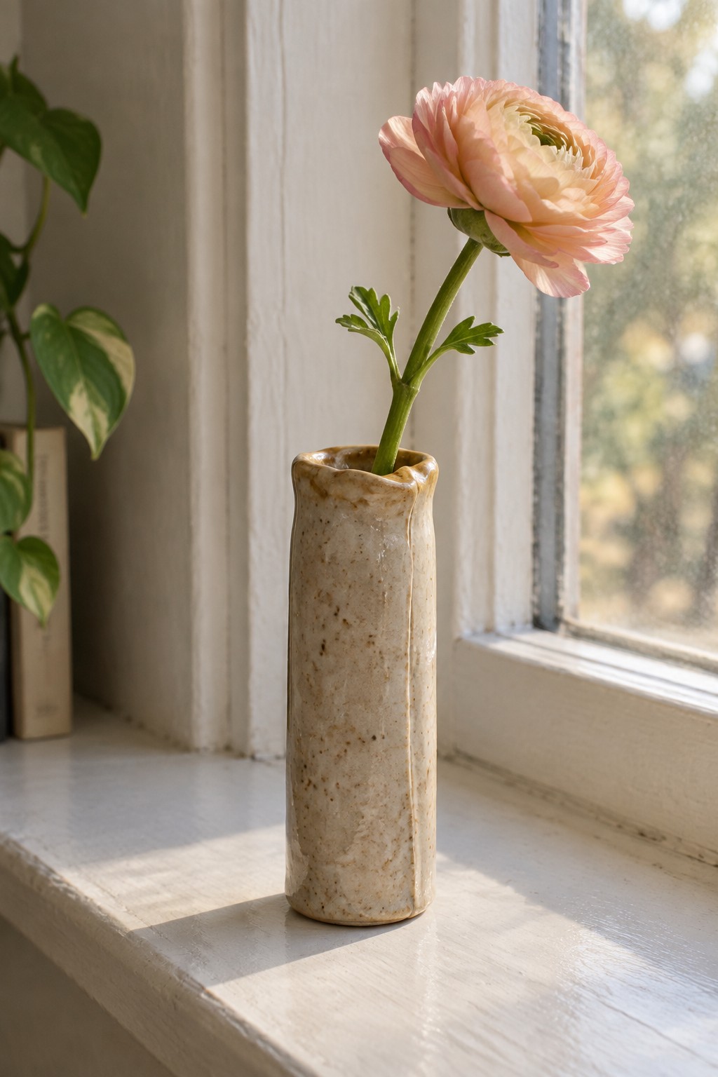 Peach ranunculus in speckled beige vase on sunlit white windowsill